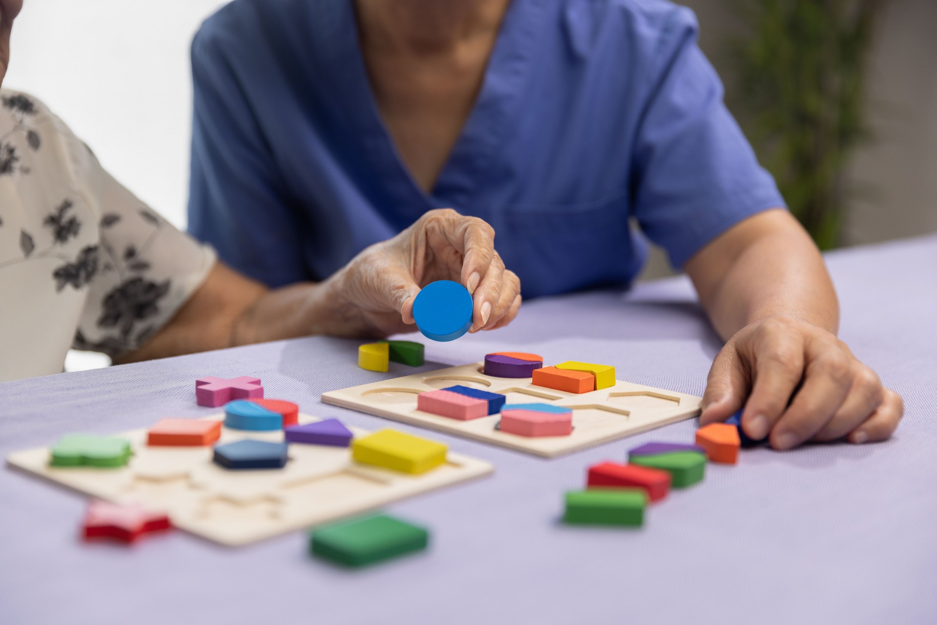 Pflegekraft und Seniorin spielen Holzform Puzzles Spiel zur Demenzprävention